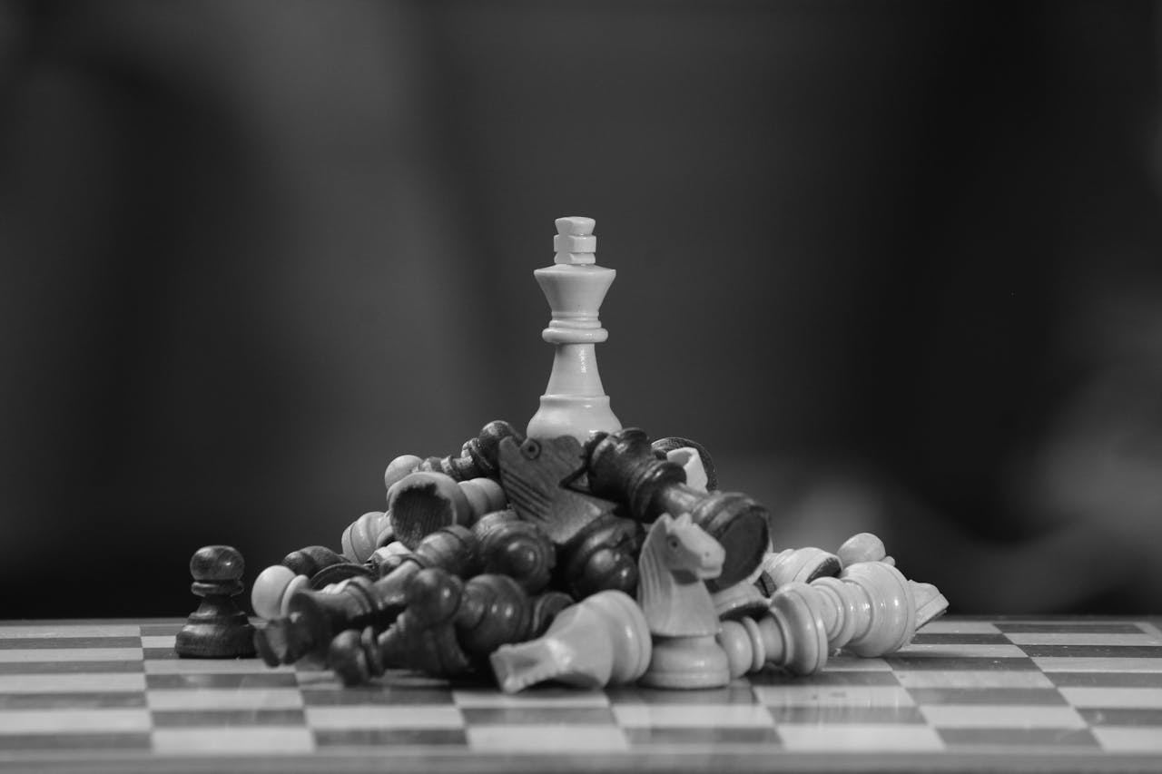 Black and white image of a chess king standing victorious amid fallen pieces on a board.