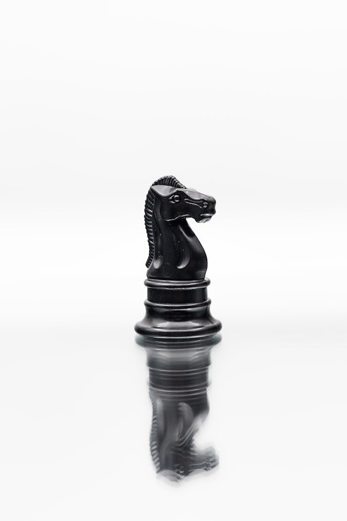 A black knight chess piece stands on a reflective surface, symbolizing strategy and intellect.