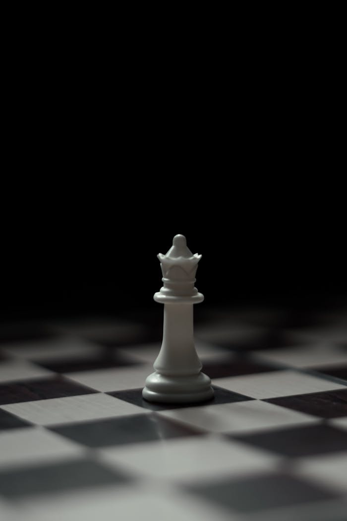 A solitary white queen chess piece on a dimly lit chessboard, symbolizing strategy.