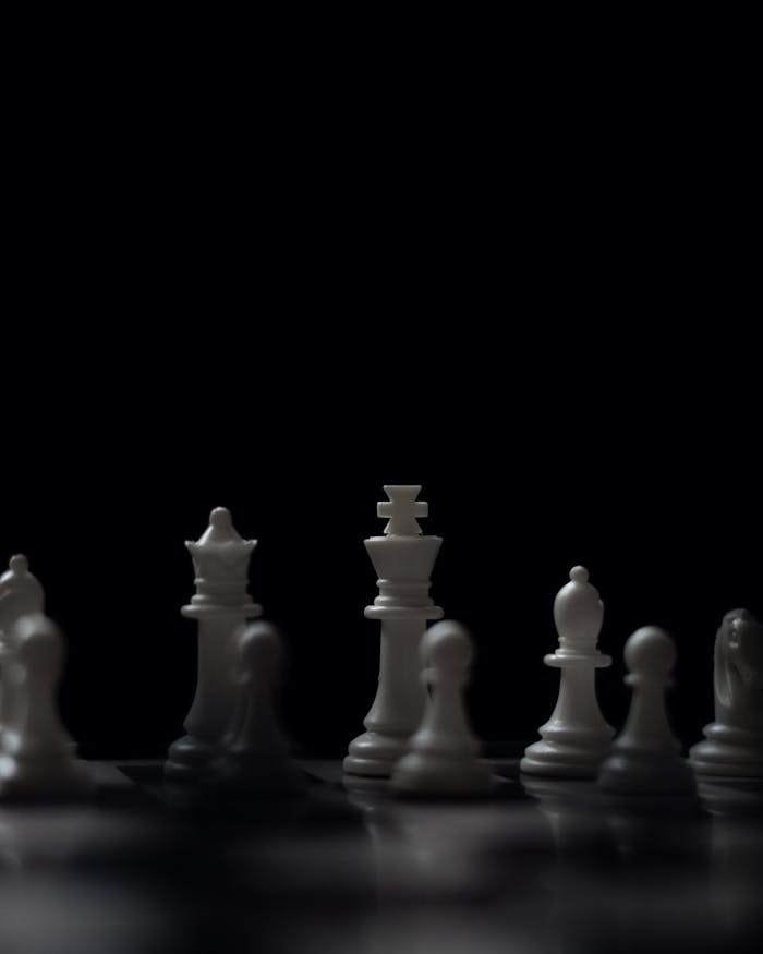 A dramatic, low-light image showcasing a chess set with white pieces prominently featured against a dark background.